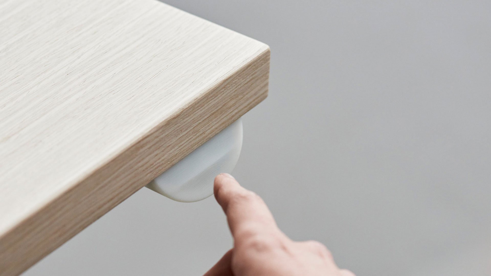 Man's hand points at small white object on wooden surface