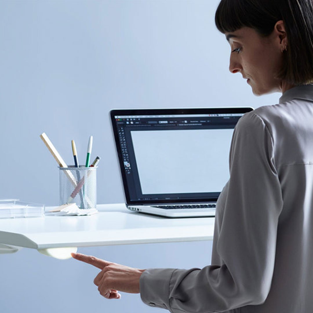 Woman in light blue blouse stands at desk with laptop and tablet
