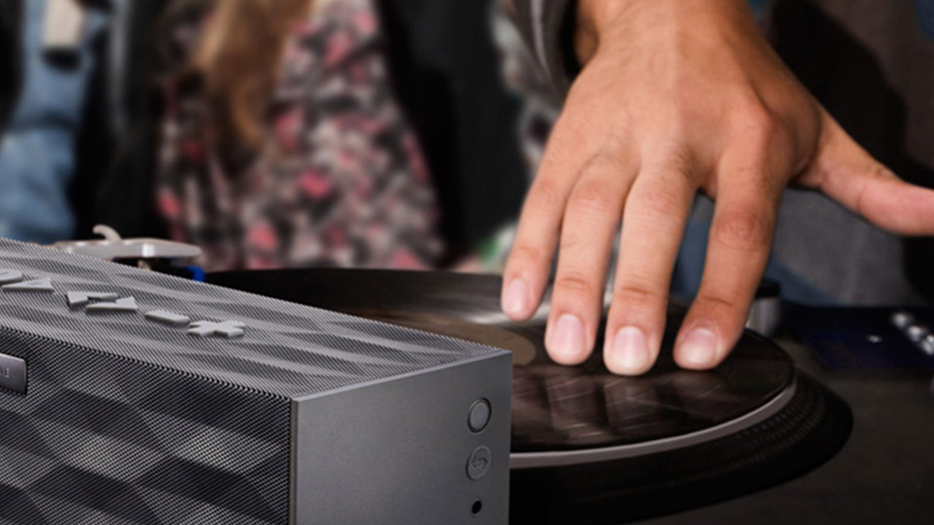 DJ scratching a vinyl turntable record next to a graphite Big Jambox wireless speaker at a Jawbone event