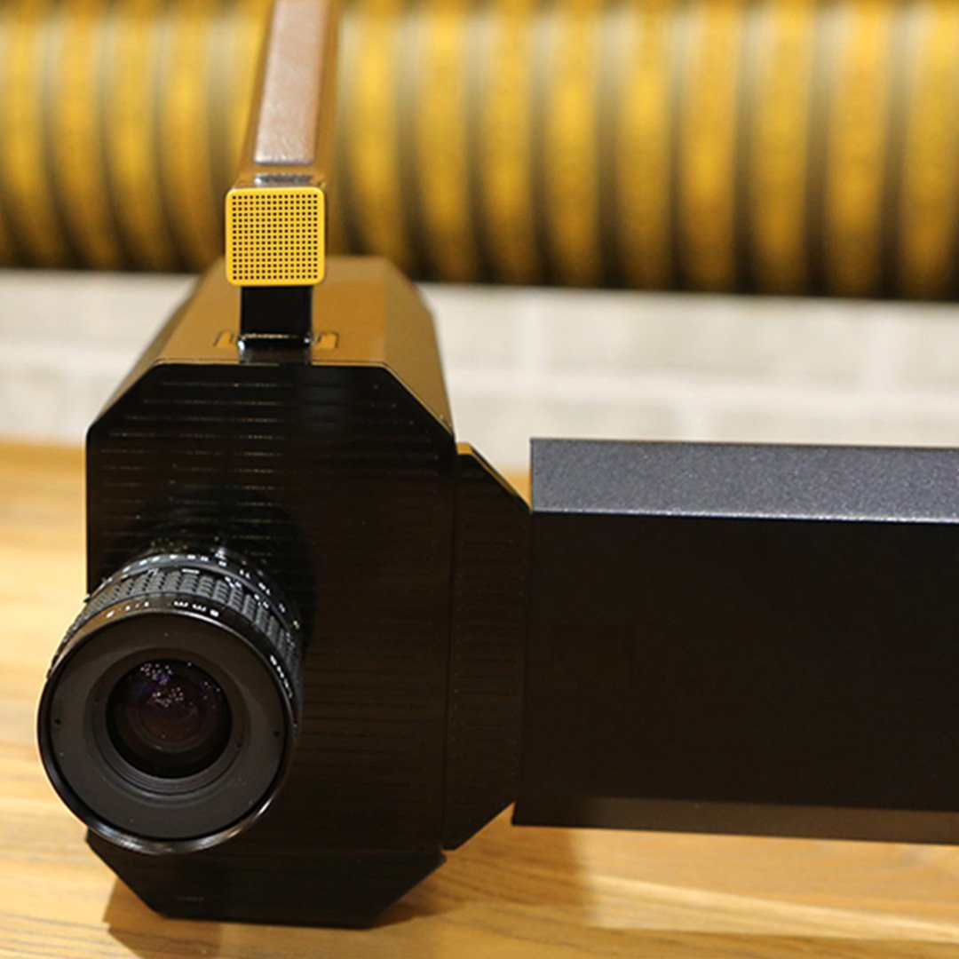 Black camera with yellow accessory on brick wall backdrop