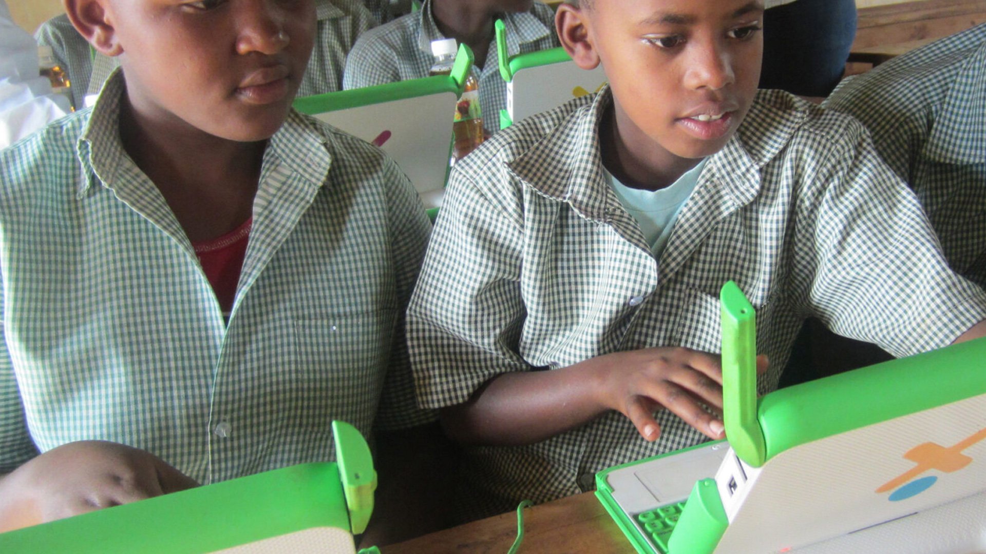OLPC XO Laptop in classroom: two children in school uniforms sitting at a table with green and white boxes