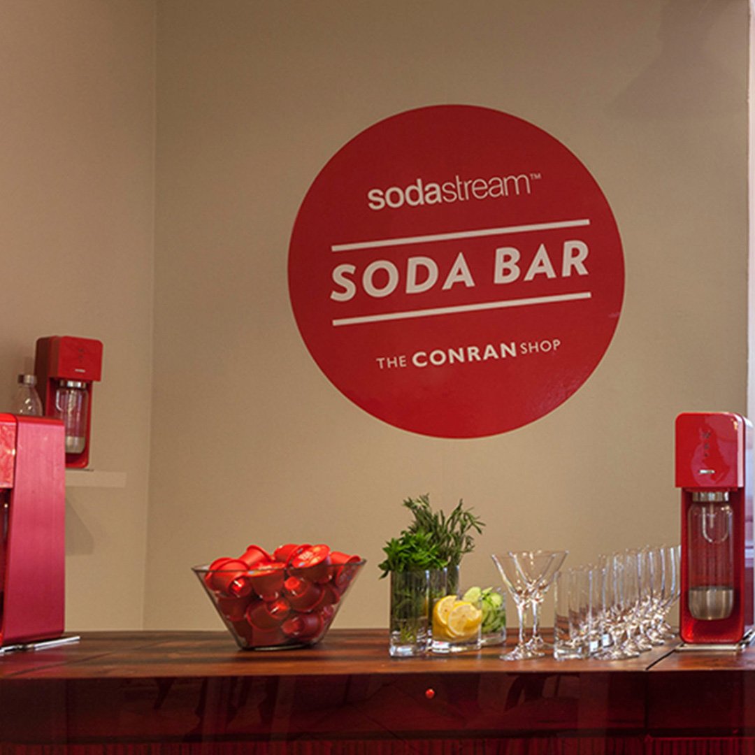 Red sign with white text reading 'SodaStream' and 'The Conran Shop', on