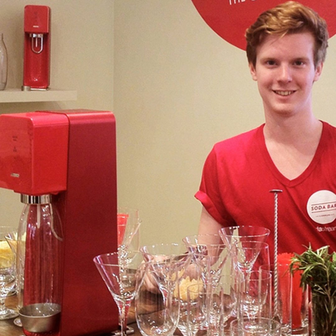 Man standing behind a counter with red coffee machine and wine glasses