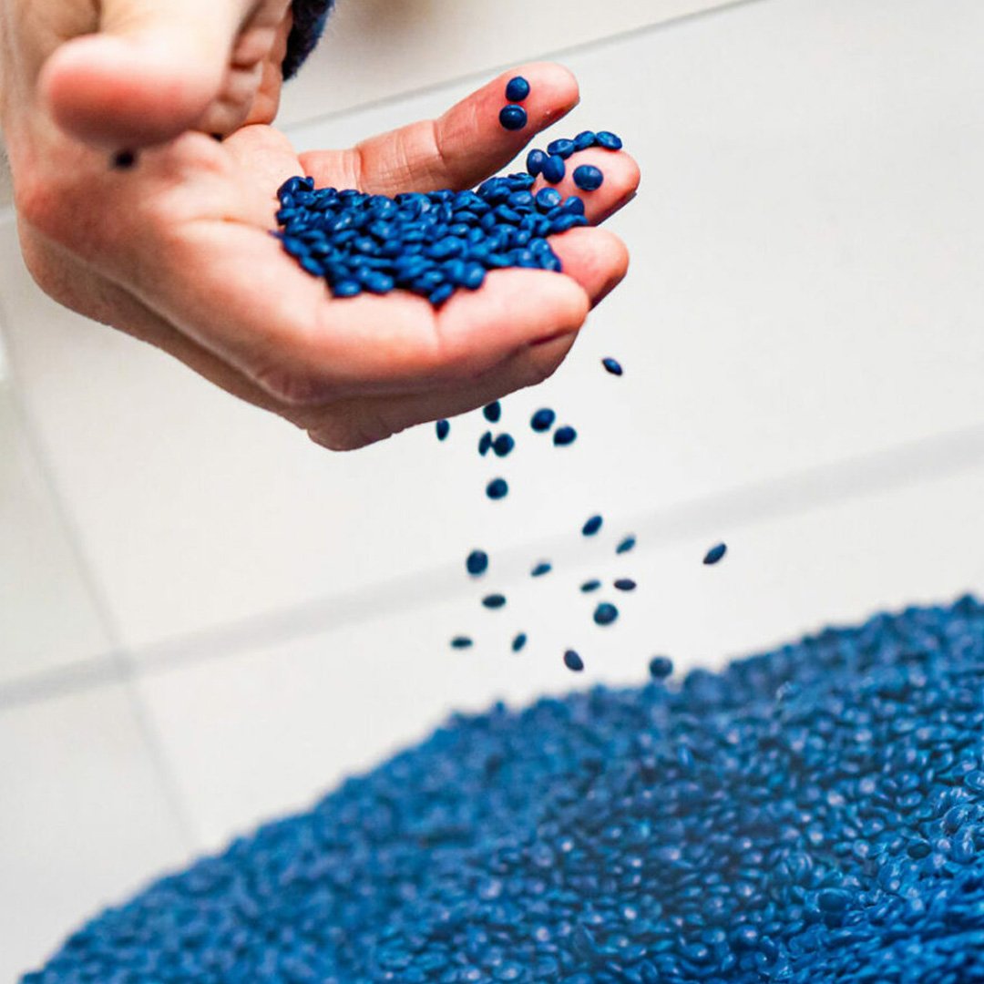 The Ocean Cleanup Sunglasses raw material: hand pouring blue recycled plastic pellets into a container