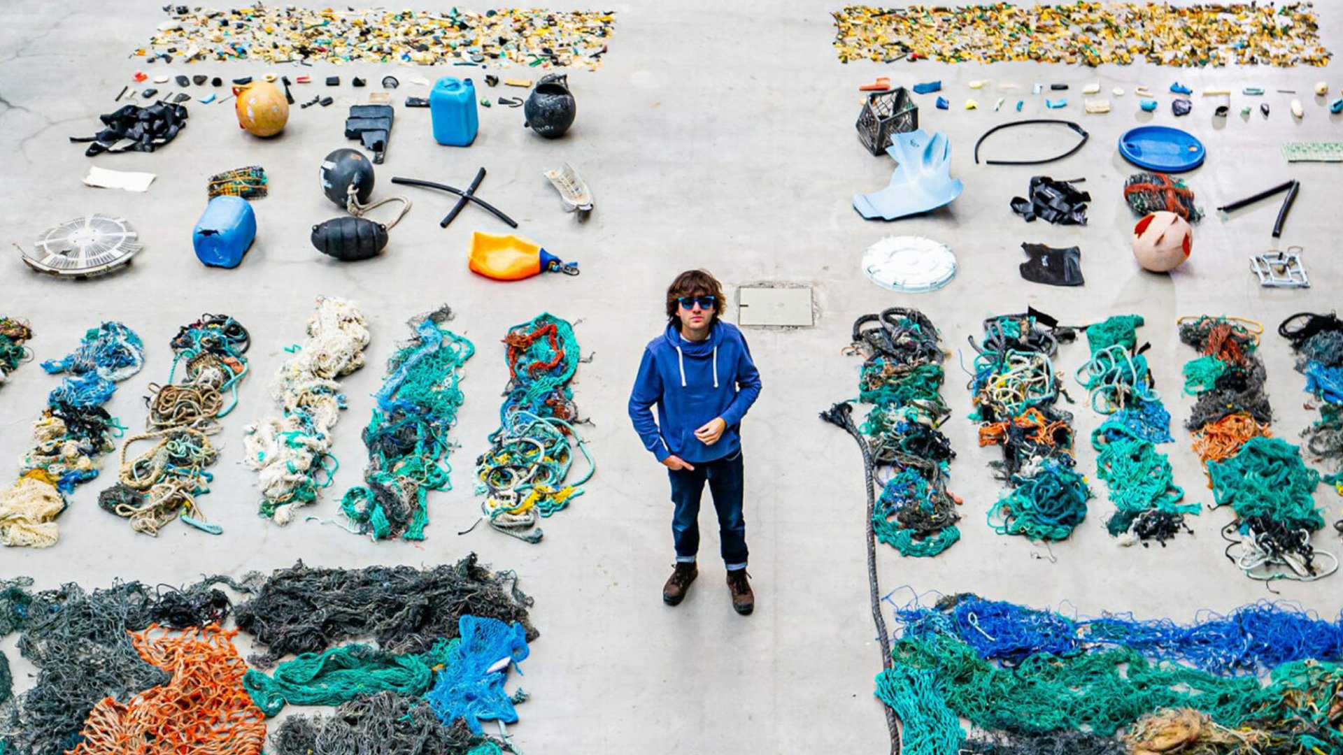 The Ocean Cleanup Sunglasses team member in blue jacket standing beside a table of collected ocean materials