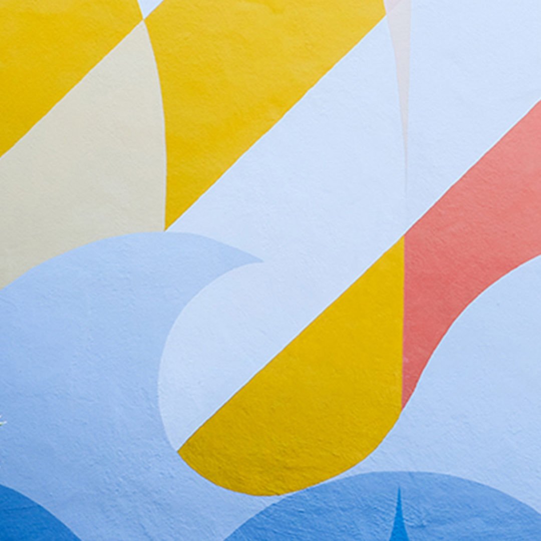 Detail of Willie Mays Boys & Girls Club mural with bold yellow sun shape, coral and pink diagonal stripes and pale blue wave