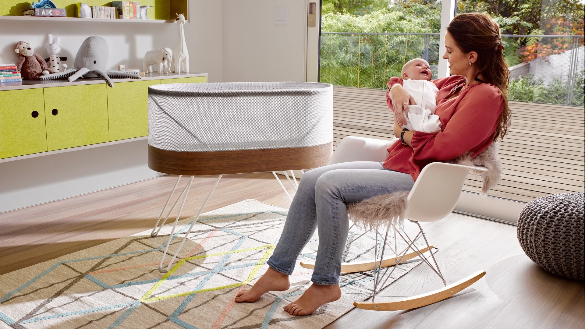 Mother holding baby beside Snoo bassinet