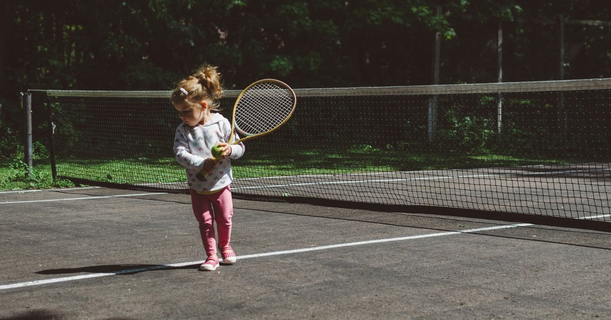 girl holding lawn tennis racket while standing beside white and black net