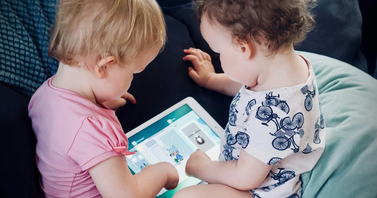 two toddlers sitting on sofa while using tablet computer