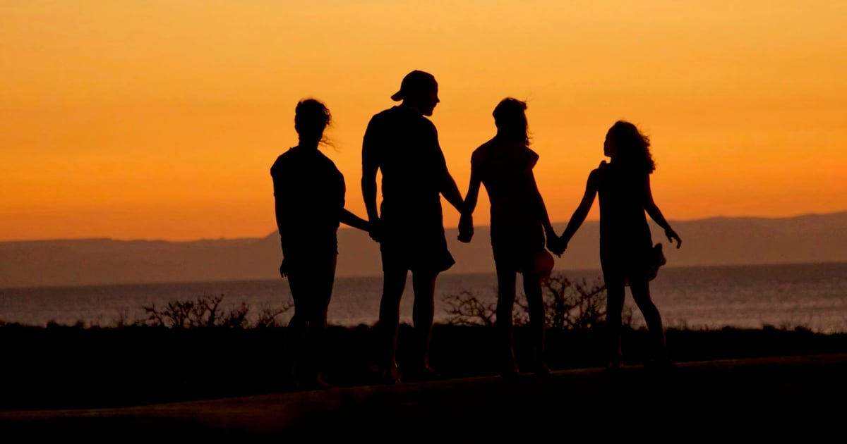 A family in silhouette holding hands against a warm orange sky by the sea