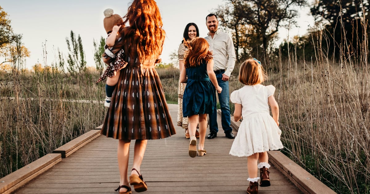 A family walking along a wooden boardwalk in a field during golden hour