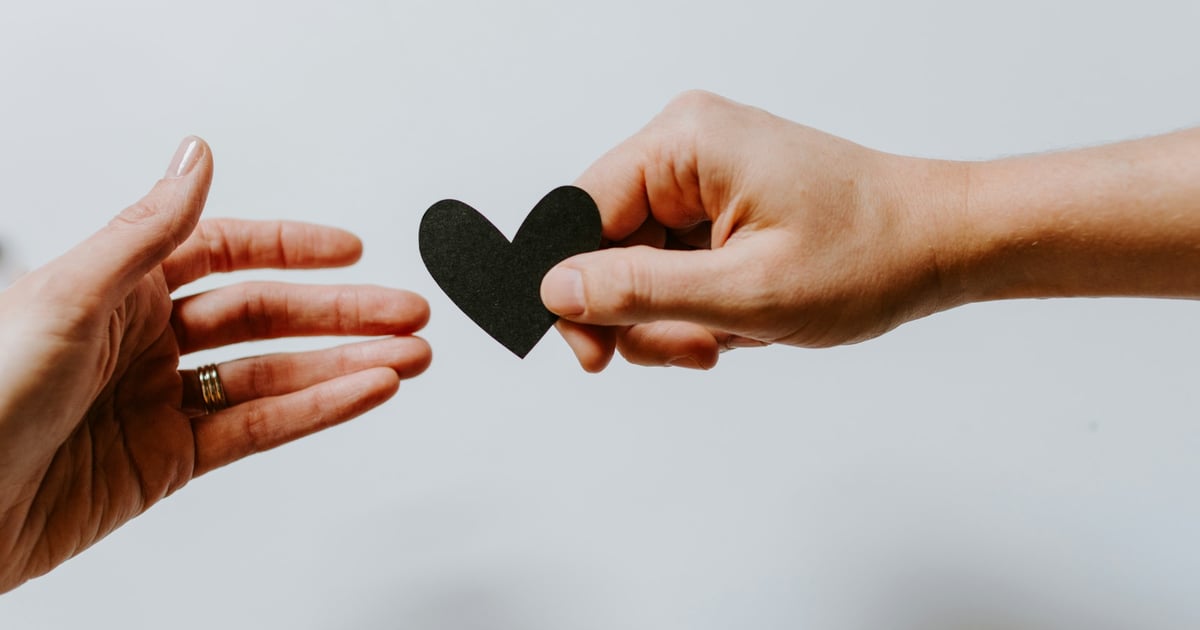 person reaching black heart cutout paper