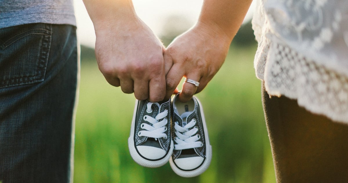 woman and man holding black crib shoes standing near green grass during daytime