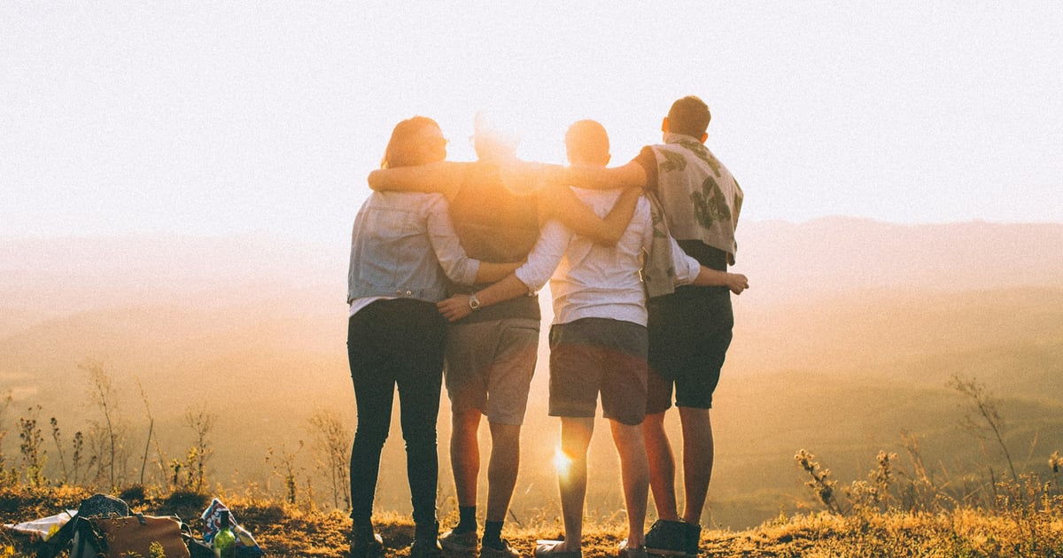 four person hands wrap around shoulders while looking at sunset