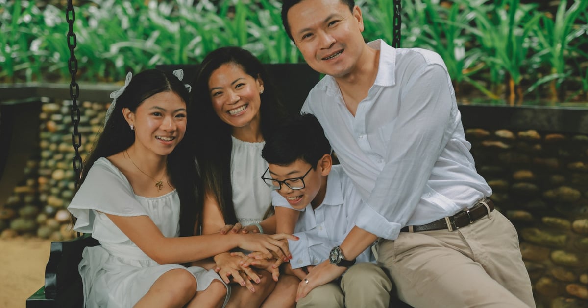 A happy family of four sitting on a swing outdoors.