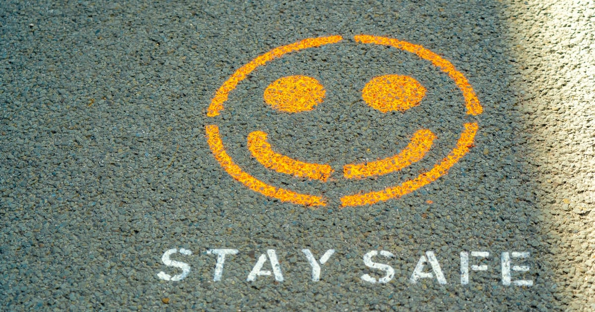 An orange spray-painted smiley face and the text STAY SAFE on grey asphalt