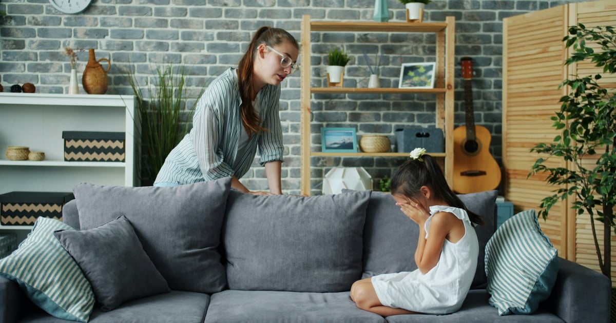 Mother scolds crying daughter on sofa in living room.