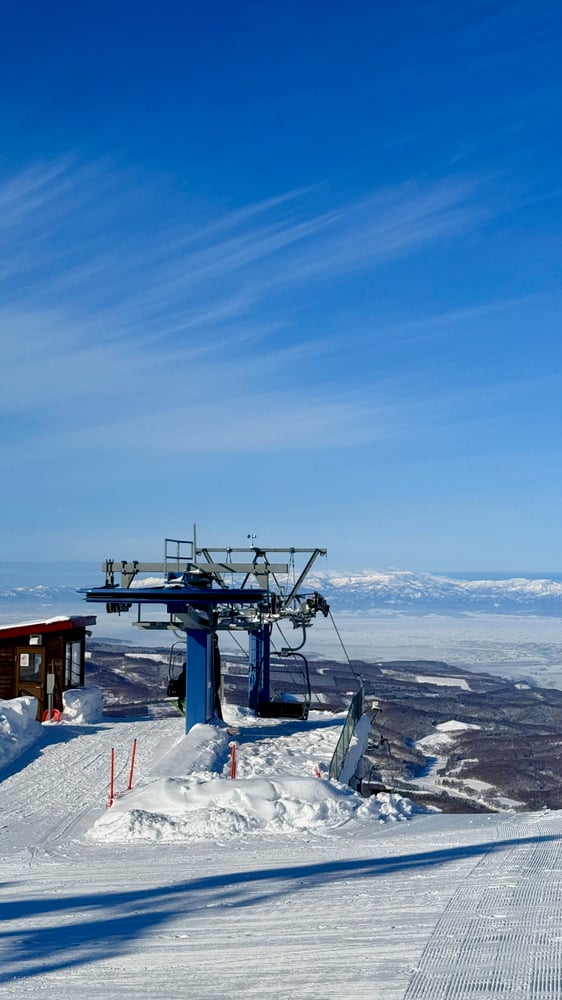 A ski lift on a snowy mountain against a clear blue sky with distant mountains in the background.