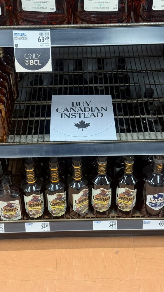The image shows an empty shelf with a sign that says 'Buy Canadian Instead' above another shelf of rum bottles in a store.