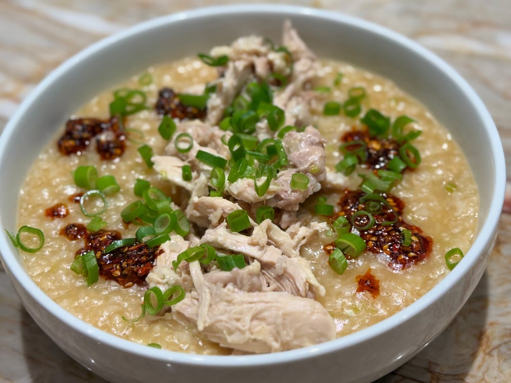 A bowl of savory porridge, topped with shredded chicken, green onions, and chili crunch.