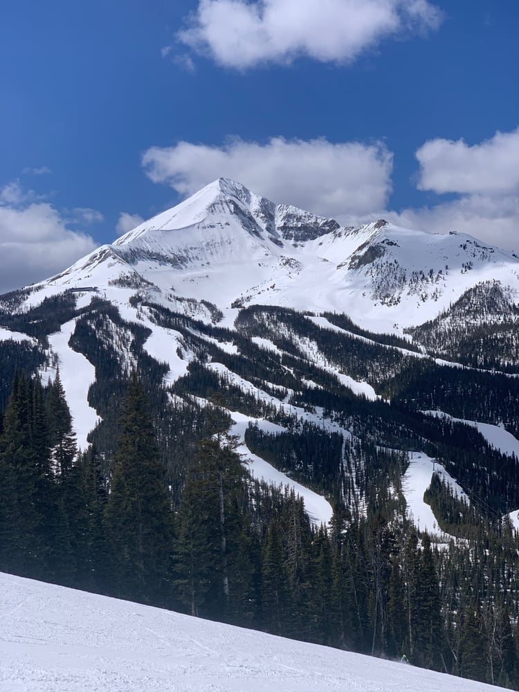 A breathtaking snowy mountain landscape with a tall, snow-capped peak rising above a forested valley covered in snow, Lone Peak in Big Sky, MT.