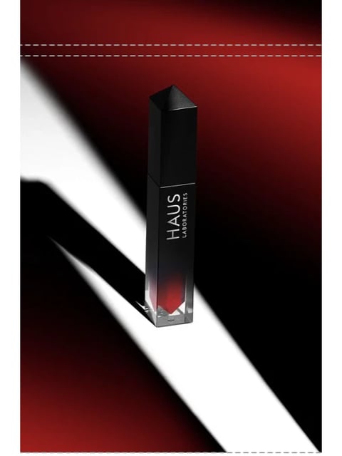 This image presents a highly stylized, photorealistic 3D render of a cosmetic product, specifically a sleek, angular lipstick or lip gloss tube. The visual aesthetic is minimalist and luxurious, employing a dramatic, high-contrast lighting setup. The dominant color language is a stark interplay between deep, velvety reds, pure whites, and profound blacks, with a saturated crimson gradient at the base of the product. Lighting is directional and hard, casting a sharp, elongated shadow from the product onto the white surface, creating a sense of dramatic tension and highlighting the product's geometric form. The texture and material feel are polished and glossy; the product's casing appears to be made of a smooth, reflective black material that transitions into a translucent red base, while the surface it rests on is a flat, matte white. Compositionally, the image uses a dynamic diagonal split between the white foreground and the dark red background, with the product placed centrally but offset by its strong shadow, creating a sense of depth and negative space. The shape language is strictly geometric and angular, featuring sharp edges, clean lines, and a faceted, crystalline cap, with no organic forms present. The overall mood and atmosphere are sophisticated, bold, and intensely modern, conveying a sense of premium quality and artistic precision through its controlled, high-impact visual style.