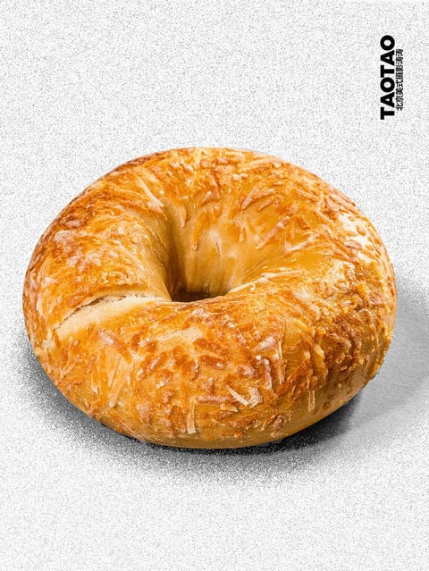 The image presents a photorealistic, high-resolution studio photograph of a single, golden-brown bagel, rendered with exceptional clarity and detail. The dominant color palette is warm, featuring rich amber and toasted honey tones on the crust, contrasted by subtle, pale beige highlights where the inner dough is exposed, all set against a neutral, cool-toned, speckled grey background that provides a clean, modern contrast. The lighting is directional and soft, likely from a large key light source positioned to the upper left, creating gentle, diffused shadows that define the bagel's rounded form and accentuate the intricate, flaky texture of the melted cheese topping without harshness. The texture is highly tactile and realistic, showcasing the crispy, slightly uneven surface of the baked cheese, the glossy sheen of the egg wash, and the soft, porous interior visible through a small split in the crust. Compositionally, the bagel is centrally framed in a close-up, top-down perspective with a shallow depth of field that keeps the entire subject in sharp focus while the background subtly recedes, emphasizing the object's three-dimensionality. The shape language is organic and soft, characterized by the bagel's imperfect, hand-formed circular form with gentle curves and no hard geometric edges. The overall mood is appetizing, clean, and inviting, conveying a sense of artisanal quality and fresh, comforting warmth through its precise, commercial food photography style.