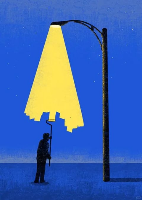 The image features a stylized, illustrative aesthetic with a flat, graphic quality and a textured, grainy finish reminiscent of a screen print or risograph. The color language is dominated by a deep, saturated cobalt blue background, contrasted sharply by a vibrant, warm yellow light cone. The lighting approach is dramatic and directional, with the yellow light appearing as a solid, geometric shape that is being 'painted' onto the scene by a silhouetted figure using a paint roller, creating a hard-edged, surreal effect. The texture is uniformly grainy across all surfaces, giving a tactile, paper-like feel. Compositionally, the scene is arranged with strong vertical and diagonal lines, featuring a tall, dark lamppost on the right and a small human figure on the left, creating a balanced but asymmetrical layout with significant negative space. The shape language is a mix of organic forms (the figure) and strict geometric shapes (the triangular light cone, the rectangular pole), with clean, defined edges. The mood is contemplative, quiet, and slightly surreal, conveying a sense of solitary creation or the artificial construction of light within a vast, dark environment.