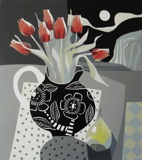 This is a still life artwork rendered in a flat, illustrative, and graphic style, reminiscent of a woodcut or linocut print. The color language is dominated by a muted, desaturated palette of cool grays, deep black, and off-white, punctuated by the warm, saturated reds of the tulip blooms and the soft, glowing yellow of a candle flame. The lighting is stylized and non-naturalistic, with the candle providing a localized, soft yellow glow that does not cast realistic shadows, contributing to a flat, compositional light. The texture is smooth and graphic, with no painterly brushstrokes; surface qualities are defined by flat color fields and bold, white line work on the black vase, creating a tactile impression of a printed or cut-paper medium. The composition is tightly framed and layered, with the patterned vase and cloth in the foreground, the flowers in the mid-ground, and a stylized window view with a moon in the background, creating a shallow, stage-like depth. The shape language is a mix of bold geometric patterns (dots, diamonds, stripes) and simplified organic forms (the tulips, leaves, vase silhouette), all defined by clean, sharp edges and consistent line weight. The overall mood is quiet, contemplative, and slightly melancholic, with a strong sense of graphic design and decorative arrangement.