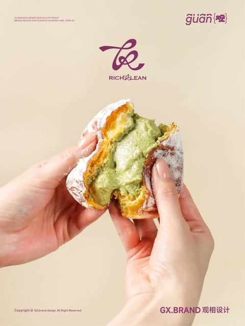 The image features a close-up, centered view of a pair of hands holding a split-open pastry, set against a solid, warm beige background. The pastry has an irregular, rounded, puffy silhouette, appearing soft and slightly deflated where it is torn. Its exterior is a golden-brown, fried dough with a matte, slightly uneven surface, generously dusted with a fine, white powdered sugar that creates a soft, powdery texture. The interior reveals a thick, creamy filling with a vibrant, muted green color, likely matcha or pistachio, which has a smooth, dense, and slightly glossy surface where it is exposed. The hands holding the pastry have a light skin tone, with neatly manicured nails painted in a soft, neutral pink polish. The lighting is soft and diffused, coming from the front-left, creating gentle highlights on the pastry's sugary surface and the creamy filling, with subtle shadows defining the contours of the hands and the pastry's interior. The overall style is realistic and appetizing, focusing on the textural contrast between the crisp, sugary exterior and the smooth, rich filling. The composition implies a moment of indulgent consumption, with the hands acting as a scale reference for the pastry's handheld size.