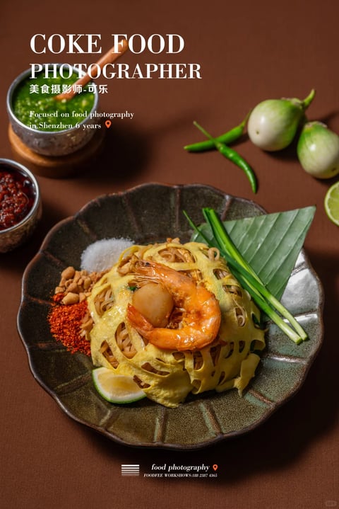 This image exemplifies a photorealistic, high-end commercial food photography style, characterized by a warm, earthy, and inviting aesthetic. The dominant color palette is anchored by rich, deep browns in the background and plate, complemented by the vibrant golden-yellow of the egg net, the warm orange-pink of the shrimp, and pops of fresh green from the chilies, lime, and scallions. The lighting is directional, appearing to come from the upper left, creating soft, diffused shadows that enhance the three-dimensionality of the dish while maintaining a warm, intimate color temperature. Textures are rendered with exceptional clarity and tactile appeal: the delicate, lacy crispness of the egg net, the glossy sheen of the shrimp, the granular texture of the chili powder and sugar, and the matte, slightly rough surface of the ceramic plate are all distinctly palpable. The composition is a centered, overhead flat lay with a shallow depth of field, focusing sharply on the main dish while gently blurring the peripheral ingredients like the eggplants and condiment bowls, creating a sense of depth and focus. The shape language is primarily organic, defined by the curved forms of the shrimp, the irregular scalloped edge of the plate, and the natural lines of the vegetables, contrasted subtly by the geometric lattice of the egg net. The overall mood is one of rustic elegance and appetizing warmth, conveying a sense of crafted, authentic culinary artistry.