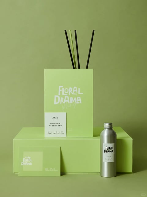 This is a photorealistic studio product photograph featuring a minimalist, monochromatic design. The dominant color palette is a vibrant, saturated chartreuse green, used for the background, product boxes, and cards, creating a cohesive, high-contrast look against the black diffuser sticks and silver bottle. The lighting is soft and diffused, likely from a large overhead or front-facing source, casting gentle, subtle shadows that emphasize the clean lines and geometric forms of the objects without creating harsh highlights. The composition is structured and balanced, with products arranged on a tiered platform to create depth and visual hierarchy, using a centered, symmetrical framing. The materials are rendered with a smooth, matte finish on the paper and cardboard, contrasting with the cool, reflective metallic surface of the aluminum bottle and the natural, porous texture of the black and green reeds. The shape language is predominantly geometric and rectangular, with sharp edges and clean lines, accented by the organic, linear forms of the diffuser sticks. The overall mood is modern, fresh, and sophisticated, conveying a sense of calm, curated elegance through its minimalist aesthetic and harmonious color scheme.