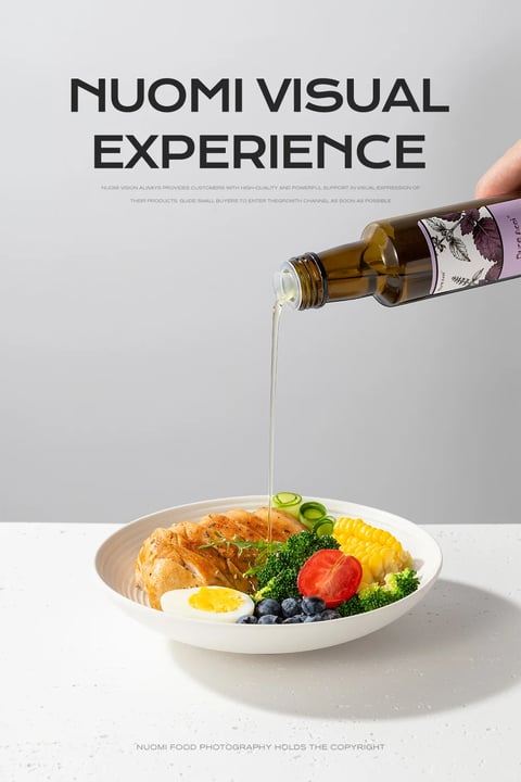 This is a high-resolution, photorealistic commercial food photography image presented in a vertical format with a clean, minimalist aesthetic. The main subject is a white, shallow ceramic bowl filled with a healthy meal, positioned slightly off-center in the lower half of the frame. The bowl contains a sliced grilled chicken breast, a halved hard-boiled egg, a cluster of blueberries, a halved cherry tomato, a piece of corn on the cob, several small broccoli florets, and thinly sliced cucumber rounds. A hand, entering from the top right, holds a dark amber glass bottle with a purple and white label featuring botanical illustrations, pouring a steady, thin stream of clear, golden oil directly onto the chicken and broccoli. The scene is set against a seamless, light grey background that transitions into a white, subtly speckled countertop surface. The overall composition is balanced, with the pouring action creating a dynamic vertical line that draws the eye from the bottle to the food. The lighting is bright, soft, and diffused, likely from a large source to the left, creating gentle highlights on the oil stream, the glossy surface of the tomato, and the moist texture of the chicken, while casting soft, subtle shadows to the right of the bowl and bottle. The color palette is vibrant and natural, dominated by the warm browns and golds of the chicken and oil, the bright greens of the broccoli and cucumber, the red of the tomato, the yellow of the egg yolk and corn, and the deep blue of the berries, all set against the neutral grey and white backdrop. Text is present at the top and bottom of the image. At the top, in large, bold, black sans-serif capital letters, it reads "NUOMI VISUAL EXPERIENCE". Below this, in much smaller, lighter grey text, is a two-line paragraph: "NUOMI VISION ALWAYS PROVIDES CUSTOMERS WITH HIGH-QUALITY AND POWERFUL SUPPORT IN VISUAL EXPRESSION OF THEIR PRODUCTS. GUIDE SMALL BUYERS TO ENTER THE GROWTH CHANNEL AS SOON AS POSSIBLE". At the very bottom, centered in small grey text, is the line "NUOMI FOOD PHOTOGRAPHY HOLDS THE COPYRIGHT". The text serves a branding and informational role, framing the image as a professional service showcase. The focus is sharp throughout the food bowl and the pouring oil, with a slightly shallower depth of field softening the background and the far edge of the countertop, emphasizing the freshness and appetizing quality of the meal. The mood is clean, healthy, professional, and aspirational, conveying a sense of premium quality and careful preparation.