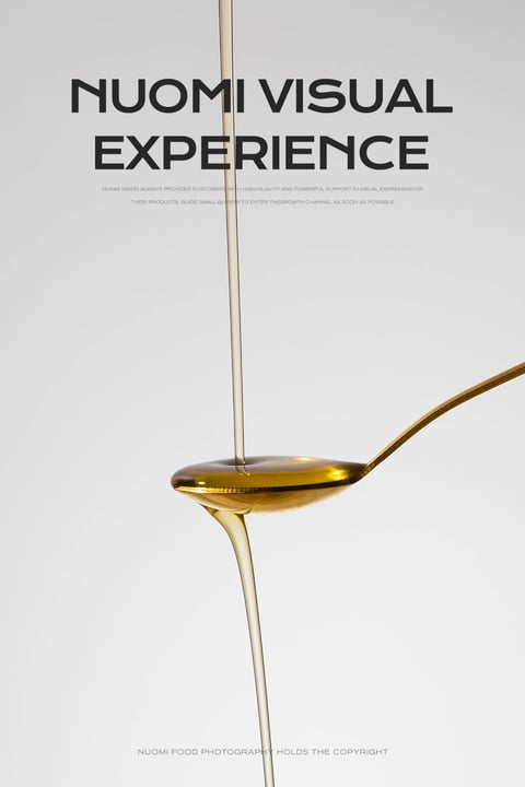 The image presents a highly stylized, photorealistic close-up of a golden liquid, likely honey or syrup, being poured onto a metallic spoon against a clean, neutral background. The composition is vertically oriented, with a thin, continuous stream of the viscous liquid descending from the top edge, striking the center of a shallow, oval spoon bowl, and then overflowing in a smooth, tapering stream from the spoon's front lip, creating a dynamic sense of motion and fluidity. The visual aesthetic is minimalist and commercial, emphasizing the luxurious texture and clarity of the subject through precise rendering. The color language is dominated by a warm, monochromatic palette of amber, gold, and honey tones, with high saturation in the liquid itself and low saturation in the background, creating strong contrast. The lighting is soft and diffused, appearing to come from the front and slightly above, producing gentle highlights on the liquid's surface and the spoon's rim while casting subtle, soft shadows that enhance the three-dimensional form without harshness. Texture and material feel are rendered with exceptional detail: the liquid appears thick, glossy, and perfectly smooth, with a glass-like transparency and viscosity, while the spoon exhibits a polished, reflective metallic surface with a subtle brushed texture. Compositionally, the image uses a tight, centered framing with significant negative space, drawing focus entirely to the interaction between the liquid and the spoon; the vertical flow of the liquid creates a strong central axis. Shape language combines the organic, flowing curves of the liquid streams with the precise, geometric oval of the spoon bowl and the clean, straight handle line. The mood is serene, elegant, and indulgent, conveying a sense of purity and high quality. Visible text appears in the upper portion: large, bold, sans-serif black text reads "NUOMI VISUAL EXPERIENCE," with smaller, light gray sans-serif text below stating, "NUOMI VISION ALWAYS PROVIDES CUSTOMERS WITH HIGH-QUALITY AND POWERFUL SUPPORT IN VISUAL EXPRESSION OF THEIR PRODUCTS. GUIDE SMALL BUYERS TO ENTER THE GROWTH CHANNEL AS SOON AS POSSIBLE." At the very bottom, in small gray text, it reads, "NUOMI FOOD PHOTOGRAPHY HOLDS THE COPYRIGHT." This text functions as branding and a tagline, framing the image as a professional visual showcase. The focus is critically sharp on the point where the liquid stream meets the pool in the spoon and on the overflowing edge, rendering the textures and light refractions with extreme clarity, while the background and the spoon's handle gently soften, directing the viewer's eye to the central action.
