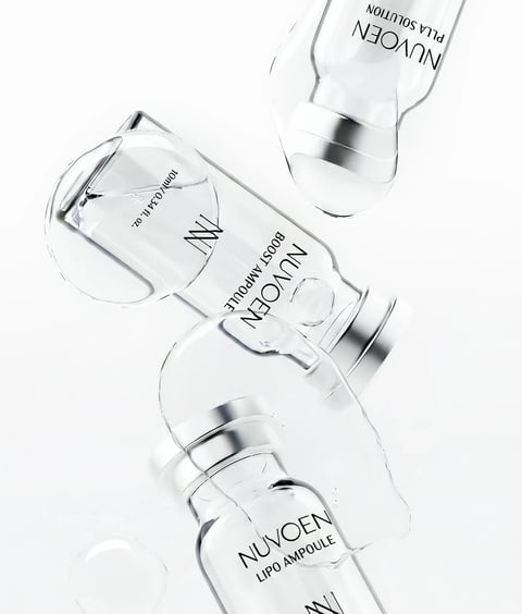The image presents a high-key, photorealistic product shot featuring three clear glass ampoules with silver metallic caps, arranged dynamically against a stark white background. The composition is diagonal and layered, with one ampoule in the foreground lying on its side, partially covered by a large, viscous, clear gel droplet that cascades over its body, while two other ampoules are positioned behind it, one upright and one tilted, creating a sense of depth and movement. Visible text on the foreground ampoule includes the brand name 'NUVOEN' in a clean, sans-serif font, followed by 'LIPO AMPOULE' below it, with a stylized 'N' logo near the bottom; the middle ampoule displays 'NUVOEN' and 'BOOST AMPOULE' with '10ml / 0.34 fl. oz.' near its top; the top ampoule shows 'NUVOEN' and 'PLLA SOLUTION'. The lighting is bright, soft, and diffused, coming from above and slightly to the side, creating crisp, clean highlights on the glass and metallic surfaces with minimal, soft shadows that enhance the three-dimensional form without adding visual weight. The color palette is monochromatic and cool, dominated by whites, silvers, and the transparent clarity of the glass and gel, with high contrast between the reflective surfaces and the matte white backdrop. The texture and material rendering emphasize the smooth, flawless glass, the polished sheen of the silver caps, and the thick, glossy, gelatinous quality of the clear droplet, which appears wet and viscous. The shape language combines the geometric, cylindrical forms of the ampoules with the organic, fluid, and irregular shape of the gel droplet, creating a contrast between structured packaging and natural, flowing material. The overall mood is clinical, luxurious, and pure, conveying a sense of scientific efficacy and high-end skincare through its minimalist aesthetic and emphasis on clarity and precision.