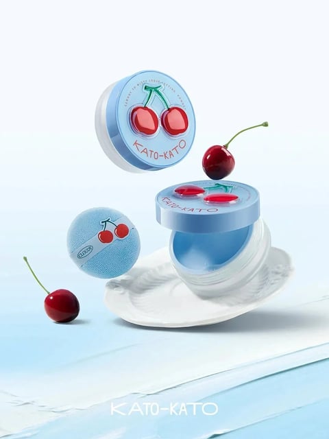 The image presents a stylized, photorealistic 3D render of a cosmetic product, specifically a loose setting powder, arranged in a dynamic, floating composition against a soft, gradient background transitioning from pale blue to white. The main subjects are two cylindrical containers of the product: one is closed and suspended in the upper left, while the other is open and resting on a white, textured, shell-like dish in the center-right, with its lid floating just above it. A matching blue powder puff with a cherry motif floats to the left of the open container. The scene is accented by two real, glossy red cherries with green stems—one positioned near the open container's lid and another in the lower left foreground. The dominant color palette is a fresh, cool combination of soft sky blue, clean white, and vibrant cherry red, with high saturation on the cherries and product accents creating a playful contrast against the muted background. The lighting is bright, soft, and diffused, coming from the upper left, casting gentle shadows that enhance the three-dimensional forms and create a clean, airy, and inviting mood. Text is prominently integrated into the product design: the brand name 'KATO-KATO' appears in a clean, red sans-serif font on the lids of both containers, curving along the lower edge. Around the top edge of the closed lid, smaller text reads 'CLOUDY TO MISTY LOOSE SETTING POWDER'. The powder puff features a white ribbon with the word 'CLOUDY' in a small, black font. The materials are rendered with a focus on tactile appeal: the containers have a smooth, matte plastic finish, the cherries are highly glossy and reflective, the powder puff has a soft, velvety texture, and the white dish has a delicate, embossed pattern. The composition uses asymmetrical balance and a shallow depth of field, with the foreground cherry slightly out of focus, to create a sense of lightness and whimsical suspension. The overall shape language blends the organic, rounded forms of the cherries and containers with the clean, geometric lines of the text and packaging, resulting in a cheerful, sweet, and modern aesthetic.
