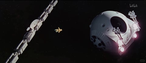The image captures a vast, deep-space exterior scene with a cosmic, star-dusted black background, evoking a sense of immense scale and isolation. The composition is dominated by two large, contrasting spacecraft and a tiny astronaut figure, arranged with strong diagonal and foreground elements. In the immediate foreground on the right, a large, white, roughly spherical spacecraft is angled toward the viewer, featuring a dark, cavernous circular opening, multiple recessed lights emitting a soft pinkish-white glow, and intricate mechanical docking clamps extending from its surface. To the left, a long, segmented, and angular space station or modular vessel stretches diagonally from the bottom-left corner into the distance, constructed from grey and white panels with visible solar arrays, antennae, and structural details. A single, small astronaut in a bright yellow suit floats in the dark void between these two massive structures, providing a stark focal point and emphasizing the scene's grand scale. The lighting is directional and cool, with the spacecraft illuminated by a soft, ambient light source that creates gentle highlights and deep, sharp shadows on their metallic and paneled surfaces, contributing to a quiet, awe-inspiring, and slightly tense atmosphere. In the top-right corner, the white text 'bilibili' is visible in a stylized, lowercase font, and in the bottom-right corner, a faint '小红书' watermark is present, both serving as platform identifiers. The overall color environment is cool, dominated by the deep black of space, the stark whites and greys of the vessels, and the single pop of warm yellow from the astronaut's suit, with subtle pink glows from the foreground ship's lights adding a touch of color temperature contrast.