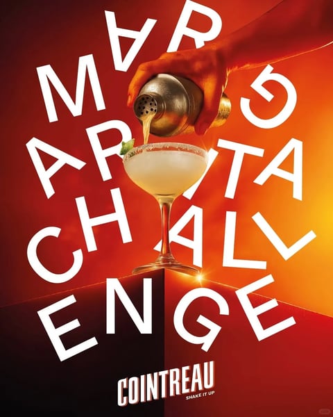 This is a vibrant, photorealistic promotional image centered on a classic Margarita cocktail being poured into a salt-rimmed coupe glass, held steady in the foreground. A hand gripping a metallic cocktail shaker, its surface reflecting warm, directional light, pours the pale-yellow drink, creating a dynamic focal point. The composition is dominated by large, bold, white sans-serif letters arranged diagonally and partially obscured by the central glass, spelling out the fragmented phrase "MARGARITA CHALLENGE." At the bottom, the word "COINTREAU" is displayed in a stylized, white, all-caps font with a subtle drop shadow, accompanied by the smaller tagline "SHAKE IT UP." The visual aesthetic is highly stylized and graphic, blending photorealistic product rendering with bold typography for a high-energy, commercial feel. The color language is intensely warm and saturated, featuring a dramatic gradient background that transitions from deep, fiery reds on the left to bright, glowing oranges on the right, with the central subject illuminated by warm, golden light that highlights the shaker's metallic texture and the cocktail's condensation. The lighting is directional and high-contrast, coming from the upper right, casting sharp shadows and creating a sense of drama and vibrancy. The texture and material feel emphasize the cold, wet condensation on the glass, the fine grain of the salt rim, the smooth metal of the shaker, and the liquid fluidity of the pouring drink, all rendered with sharp, tactile clarity. The composition uses a dynamic diagonal arrangement, with the text elements and the pouring action creating a sense of movement that frames the central, static glass, adding depth through the layered text and the distinct foreground/background separation. The shape language combines the organic curves of the glass, hand, and liquid with the strong, geometric, diagonal lines of the bold text, creating a tension between fluidity and structure. The mood and atmosphere are energetic, festive, and inviting, conveying the excitement of a cocktail challenge with high visual weight and a celebratory tone.