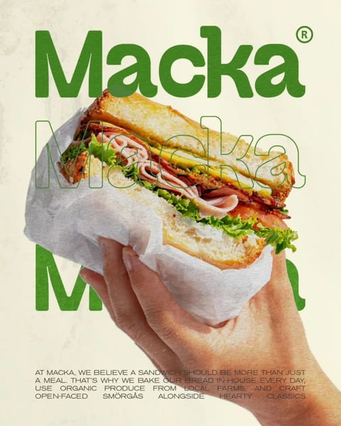 The image is a photorealistic advertisement for a sandwich brand named "Macka." The central subject is a hand holding a large, appetizing sandwich wrapped in crinkled white parchment paper. The sandwich is a long baguette-style roll, sliced open to reveal layers of ingredients including thinly sliced meats, lettuce, a pickle spear, and a sauce, all contained within a golden-brown, textured bread crust. The composition is centered, with the hand entering from the bottom right, holding the sandwich at a diagonal angle against a subtle, textured off-white background. The text "Macka" appears three times: prominently at the top in large, bold, dark green sans-serif letters with a registered trademark symbol; as a semi-transparent, outlined overlay directly on the sandwich; and partially visible in a very large scale at the bottom left. A block of smaller, dark green text at the bottom reads: "AT MACKA, WE BELIEVE A SANDWICH SHOULD BE MORE THAN JUST A MEAL. THAT'S WHY WE BAKE OUR BREAD IN-HOUSE EVERY DAY, USE ORGANIC PRODUCE FROM LOCAL FARMS, AND CRAFT OPEN-FACED SMÖRGÅS ALONGSIDE HEARTY CLASSICS." The visual aesthetic is clean and modern with a tactile, organic feel, emphasized by the paper texture and the detailed rendering of the bread and fresh ingredients. The color palette is dominated by the warm beige and gold of the bread and background, the vibrant green of the brand name and lettuce, and the varied pinks and browns of the sandwich fillings, creating a high-contrast, appetizing look with soft, natural-looking lighting that casts gentle shadows, enhancing the three-dimensional form of the hand and sandwich.