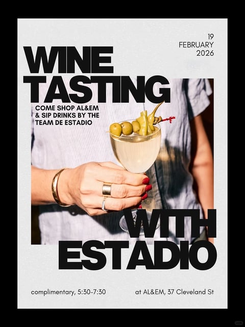 The image is a promotional poster with a dominant vertical rectangular format, featuring a central photograph overlaid with bold, graphic text. The photograph shows a close-up of a person's hand holding a coupe glass filled with a pale, creamy cocktail, garnished with a skewer of green olives and peppers; the hand has red nail polish and wears a gold cuff bracelet and two rings, set against the person's torso in a light blue striped shirt. The visual aesthetic blends photorealistic elements with a flat, graphic design style, using a high-contrast color language dominated by the crisp white background, deep black text, and the natural tones of the photograph (skin, glass, olive green, blue shirt). Lighting in the photograph appears to be a direct, hard flash, creating sharp shadows and bright highlights that emphasize texture and give a vintage, snapshot feel. Textural contrasts are prominent: the smooth, glossy glass and liquid, the tactile fabric of the shirt, the metallic sheen of the jewelry, and the grainy, matte finish of the poster's white background. Compositionally, the text is arranged in a bold, blocky manner, with 'WINE TASTING' at the top and 'WITH ESTADIO' at the bottom, framing the central image and creating strong horizontal and vertical lines that intersect with the organic shapes of the hand and glass. The shape language is a mix of the organic, rounded forms of the hand and olives and the sharp, geometric sans-serif letterforms. Smaller text provides event details: '19 FEBRUARY 2026' in the top right; 'COME SHOP AL&EM & SIP DRINKS BY THE TEAM DE ESTADIO' below the main title; and 'complimentary, 5:30-7:30 at AL&EM, 37 Cleveland St' at the bottom. The overall mood is modern, chic, and slightly retro, evoking a sophisticated yet casual social event atmosphere.