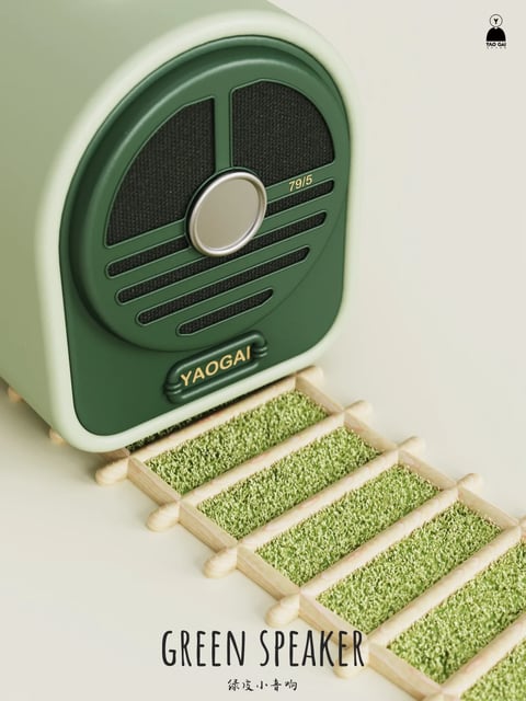 This image features a photorealistic, stylized 3D rendering of a retro-inspired green speaker positioned above a series of green, textured rectangular elements resembling steps or a track. The speaker, with a rounded rectangular form and a prominent circular speaker grille, is rendered in two shades of green: a lighter, pastel mint green for the main body and a deeper forest green for the front panel and grille details. The grille has a black mesh texture and includes a central, smooth, silver-colored circular dial. The scene is composed with the speaker angled slightly, creating diagonal lines that lead the eye down to the series of rectangular steps below, which are framed in a light wood-like material and filled with a green, grassy or moss-like texture. The lighting is soft and diffused, coming from the upper left, casting gentle shadows that emphasize the speaker's rounded edges and the texture of the steps, contributing to a calm, clean, and slightly whimsical atmosphere. The color palette is dominated by muted greens, with accents of light wood, silver, and black, creating a harmonious and earthy feel with low contrast. The composition uses a shallow depth of field, keeping the speaker in sharp focus while the background remains a soft, neutral off-white. Visible text includes the brand name "YAOGAI" in a stylized, embossed font on a dark green badge on the speaker's lower front, the number "79/5" in small, light-colored text on the upper right of the speaker grille, a logo in the top right corner with the text "YAO GAI" below a stylized icon, and the words "GREEN SPEAKER" in a handwritten-style font at the bottom center, with the Chinese characters "绿皮小音响" (meaning 'green skin small speaker') below it in a smaller, simpler font.