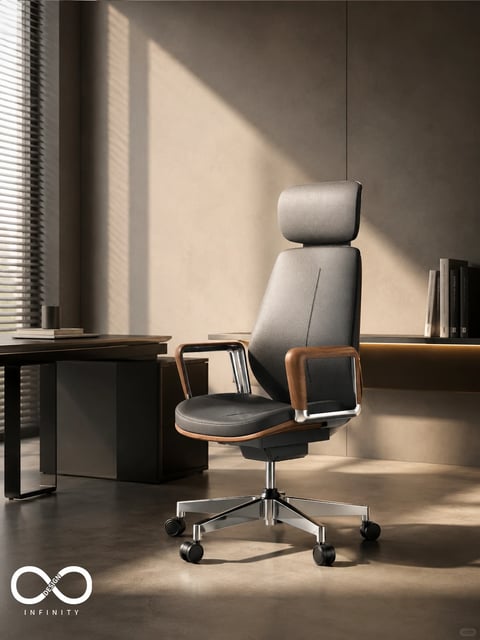 The image presents a high-end, photorealistic 3D rendering of a modern executive office chair as the central subject, positioned in a minimalist, contemporary office setting. The chair features a high back with a separate headrest, upholstered in a textured, dark charcoal or black leather-like material with visible stitching, and is accented by warm, polished wooden armrests with chrome metal supports, set atop a five-point polished chrome base with black casters. The composition places the chair slightly off-center in a medium shot, with a dark wood and metal desk partially visible to the left, holding a book and a metallic cup, and a built-in shelf with vertically arranged books in the background to the right. The lighting is dramatic and directional, coming from a large window with horizontal blinds on the left, casting soft, elongated shadows and creating a warm, golden-hour glow that highlights the chair's contours and textures against the muted, neutral beige and taupe walls. The color palette is dominated by warm neutrals, deep charcoals, and rich wood tones, with high contrast between the sunlit areas and the deep shadows. The visual aesthetic is sleek, sophisticated, and tactile, emphasizing material quality through detailed rendering of leather grain, wood polish, and metallic sheen. The mood is calm, focused, and luxurious, evoking a sense of quiet productivity. In the bottom left corner, there is a white logo consisting of an infinity symbol above the text 'DESIGN INFINITY' in a clean, sans-serif font, serving as a brand watermark.