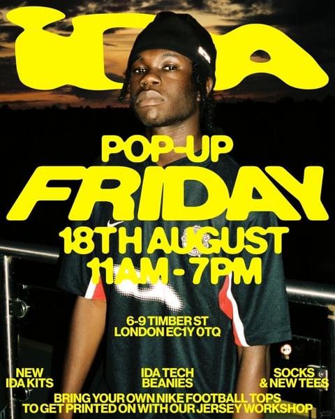 This is a vibrant, photorealistic event poster featuring a central male subject in a medium shot, posed confidently against a dark, out-of-focus background that suggests an urban or outdoor setting at dusk. The composition is layered, with bold, graphic text overlays creating a dynamic, collage-like effect. The dominant visual aesthetic is a blend of contemporary streetwear photography and high-contrast graphic design, with a strong, flat rendering of text against the photographic image. The color language is defined by a high-contrast palette: the deep blacks and dark greens of the subject's clothing and background are punctuated by the intense, saturated primary yellow of the typography and the crisp red and white accents on his shirt sleeves. The lighting is directional and dramatic, appearing to come from the upper left, casting strong highlights on the subject's face, the Nike logo, and the folds of his shirt, while leaving the right side and background in deep shadow, creating a moody, high-contrast look. Textural contrasts are key: the smooth, matte finish of the large yellow graphic letters contrasts with the fabric weave of the subject's football jersey and the slight sheen on his skin. The composition follows a clear vertical hierarchy, with the large "IDA" logo at the top, the subject in the middle, and stacked informational text below, creating a balanced yet energetic layout. Shape language is a mix of organic (the subject's form, dreadlocks) and bold geometric forms (the blocky, sans-serif typography with rounded edges). The overall mood is energetic, cool, and promotional, conveying a sense of urban style and exclusive community event. The prominent yellow text reads "IDA," "POP-UP FRIDAY," "18TH AUGUST 11AM - 7PM," "6-9 TIMBER ST LONDON EC1Y 0TQ," and lists offerings like "NEW IDA KITS," "IDA TECH BEANIES," and "SOCKS & NEW TEES," with a final call to action to "BRING YOUR OWN NIKE FOOTBALL TOPS TO GET PRINTED ON WITH OUR JERSEY WORKSHOP."