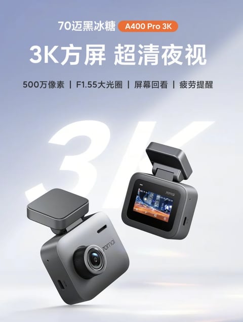 This is a promotional product image featuring two 70mai A400 Pro 3K dash cameras, one showing its front lens and the other its rear screen, floating against a soft gradient background. The composition is centered and balanced, with the cameras positioned dynamically to showcase both sides, and a large, faint '3K' graphic in the background creating depth. The visual aesthetic is clean, modern, and photorealistic, resembling a high-quality 3D product render. The color language is dominated by cool, muted tones: a gradient background shifting from light blue-grey at the top to soft white at the bottom, with the cameras rendered in matte dark grey and silver metallic finishes. The lighting is soft and diffused, appearing to come from the upper left, creating gentle highlights on the camera bodies and subtle shadows that enhance their three-dimensional form without harsh contrast. The texture and material feel are smooth and precise, with the matte plastic and brushed metal surfaces rendered realistically to convey a premium, durable quality. The shape language is distinctly geometric, characterized by the cameras' rectangular bodies, sharp edges, and circular lens, emphasizing a functional, tech-oriented design. The mood and atmosphere are professional, sleek, and focused on clarity and technological sophistication. Visible text includes the large headline '70迈黑冰糖 A400 Pro 3K' at the top in white and an orange badge, followed by the sub-headline '3K方屏 超清夜视' in large white characters. Below this, a line of smaller white text lists features: '500万像素 | F1.55大光圈 | 屏幕回看 | 疲劳提醒'. The brand name '70mai' is also visible on the camera bodies. The focus is clearly on the product itself, with the cameras rendered in sharp detail against the softly blurred background, and the text strategically placed to inform without overwhelming the visual. The background '3K' text is out of focus, further directing attention to the crisp product imagery.