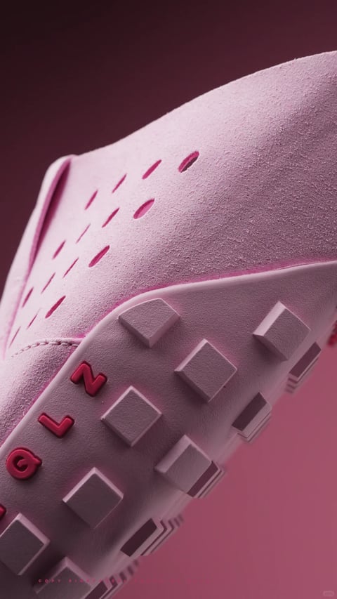 This image is a high-resolution, photorealistic 3D render featuring a dynamic close-up view of a pink footwear item, likely a contemporary clog or slip-on shoe, angled diagonally from the lower left to the upper right. The composition is tightly framed, focusing on the textured upper material and the chunky, studded sole, with a soft-focus background in a gradient of deep magenta to dusty rose. The visual aesthetic is modern and tactile, emphasizing material detail and geometric form. The dominant color palette is monochromatic, centered on soft, dusty pinks and mauves, with a muted, low-contrast saturation that creates a gentle, cohesive look. Lighting is soft and directional, appearing to come from the upper left, casting subtle shadows that define the shoe's contours and the texture of its surface, enhancing the three-dimensional feel without harshness. The material rendering is highly detailed, with a fine, granular, almost suede-like texture on the shoe's upper, contrasting with the smoother, matte rubber of the sole. The composition utilizes a shallow depth of field, keeping the foreground sole and mid-section of the shoe sharp while the background and the shoe's far edge blur softly. The shape language is a mix of organic curves in the shoe's silhouette and strong geometric elements in the square studs of the sole and the precise, elongated perforations on the upper. There is no obvious readable text or script visible in the image. The mood is calm, sophisticated, and slightly abstract, focusing on form and texture rather than narrative.