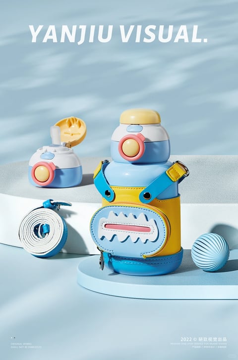 The image showcases a playful, robot-themed children's water bottle set in a stylized, bright studio scene with soft blue tones and subtle leaf shadow patterns in the background. The primary subject is a large, blue and yellow water bottle with a detachable, zippered pouch designed to look like a robot's torso, featuring a light blue belly panel with white jagged teeth-like details and a pink rectangular 'mouth' detail. The bottle itself has a rounded, tiered form with a white and light blue upper section, a large pink button, and a smooth yellow cap. To its left, a smaller, matching bottle top with a flip-up straw sits separately, showcasing the functional drinking mechanism. A coiled, white and blue woven strap with blue hardware lies in front of this smaller piece. The items rest on light blue and grey geometric platforms, with a light blue, ribbed sphere to the right, adding to the playful, modern aesthetic. The visible text includes large, bold, white sans-serif letters reading 'YANJIU VISUAL.' at the top center, and smaller white text in the bottom left corner stating 'ORIGINAL WORKS SHALL NOT BE EMBEZZLED' and in the bottom right corner reading '2022 © 研玖视觉出品' along with smaller service descriptions, indicating the image is a professional product visualization or advertisement. The objects feature a mix of matte and glossy finishes, with the bottle body showing a slight gloss, the cap and pouch appearing matte, and the strap having a woven texture. The construction details are clean, with visible stitching on the pouch, metal zipper pulls, and plastic button and strap hardware. The color scheme is a cohesive pastel palette of light blue, soft yellow, white, and coral pink, creating a cheerful, youthful, and futuristic yet soft style. Functional cues are clear: the flip-up straw, the large push-button mechanism, and the wearable pouch with a strap suggest it is designed for easy carrying and use by children.