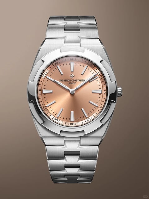 The image presents a high-resolution, photorealistic studio portrait of a luxury wristwatch, specifically a Vacheron Constantin Overseas model, set against a smooth, neutral gradient background that transitions from a muted brownish-grey to a lighter, warm taupe. The watch is positioned vertically, centered in the frame, showcasing its integrated bracelet and case design in a symmetrical, head-on composition. The overall form is a modern, integrated sports watch silhouette with a tonneau-like case shape that flows seamlessly into the bracelet. The case and bracelet are crafted from stainless steel, exhibiting a sophisticated mix of finishes: the main surfaces of the case and bracelet links feature a fine vertical brushing, while the iconic six-sided bezel, inspired by the Maltese cross, is highly polished, creating a sharp contrast. The dial is a warm, sunburst-finished salmon or copper tone, with a radial gradient that catches the light. Visible text on the dial includes the brand name "VACHERON CONSTANTIN" and "GENEVE" printed in a crisp, sans-serif font below the 12 o'clock position, along with a small Maltese cross logo. An outer minute track with Arabic numerals at five-minute intervals (e.g., 05, 10, 15... 60) and hash marks encircles the dial, with the words "SWISS MADE" subtly placed at the very bottom near the 6 o'clock marker. The watch features applied, rectangular hour markers with luminous inserts, matching the dauphine-style hour and minute hands, and a thin, straight seconds hand. Functional cues include the screw-down crown at the 3 o'clock position with protective guards and the articulate, multi-link bracelet designed for comfort. The style is decidedly modern luxury with a sporty-elegant aesthetic, emphasizing precision engineering and high-end finishing, with the context implying a premium accessory for formal or business-casual wear.