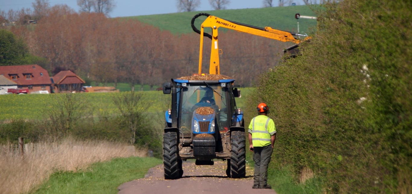Tractor hedgecutting a tall roadside hedge