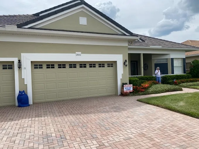 This is an image fromJohns Painting And Pressure Washing company, located in Clermont, FL. The image is a freshly painted light green and white single-story home with three-car garage by John's Painting and Pressure Washing