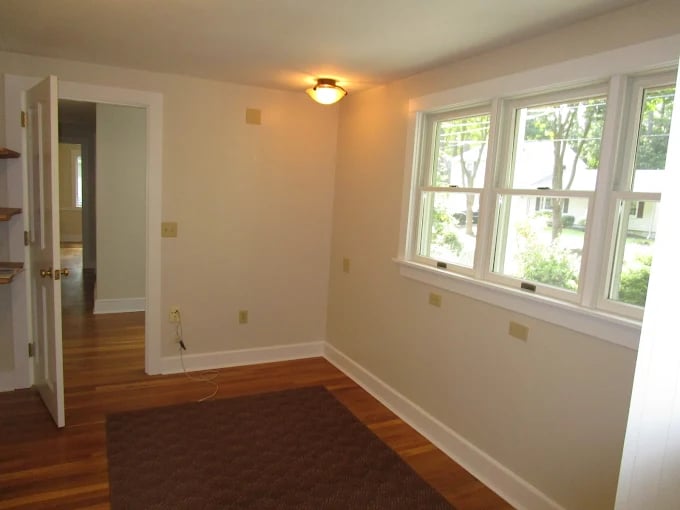 This is an image from CertaPro Painters of Woburn, Massachusetts. The photo shows a bright interior room with beige painted walls, white trim, and polished hardwood floors, highlighting the company’s interior painting services.